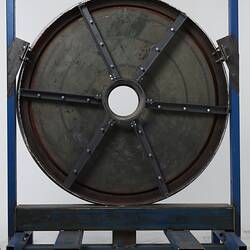 Dark disc with hole in centre. Black metal frame. Housed in blue metal rack.