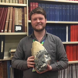 Man holding rock standing in front of shelf of books.
