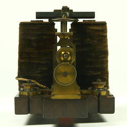 Brass apparatus with battery in centre on wooden base.
