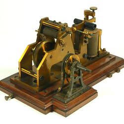 Brass apparatus with batteries on wooden base, three quarter view.