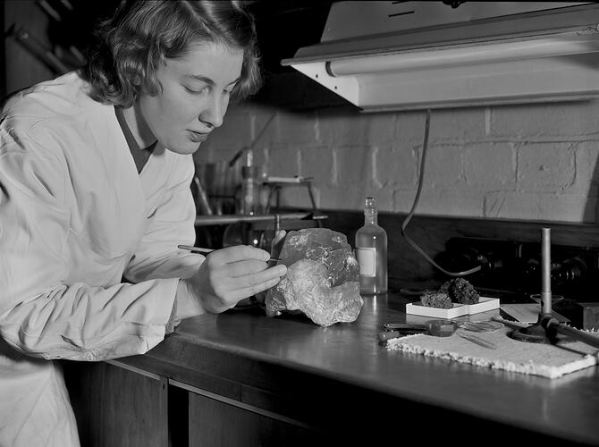A woman in a lab coat writes on a rock specimen.