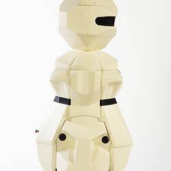Side view of cream plastic robot with angular human-like shape, ie. head, shoulders, waist and legs. Black plastic features.