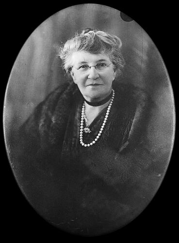 Portrait of older woman wearing glasses and a pearl necklace.