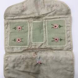Embroidered needle book, open, showing front side with pockets.