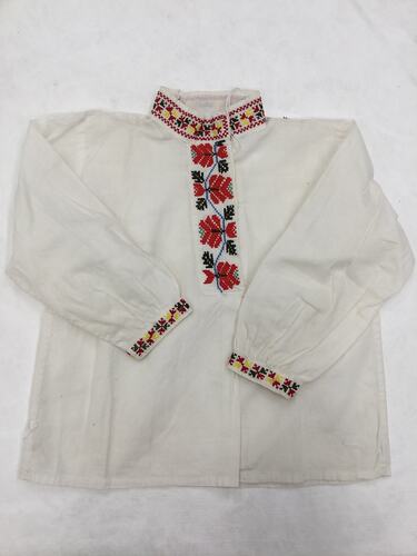 White cotton, long-sleeved shirt. Red, yellow, green, blue embroidered details on collar, cuffs and down front