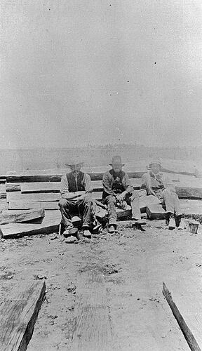 [Three men sitting on a stack of railway sleepers, circa 1925.]