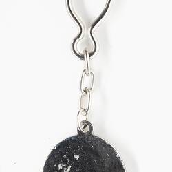 Back of metal keyring, upsidedown black horseshoe shape with central disc. Silver clip ring at top.