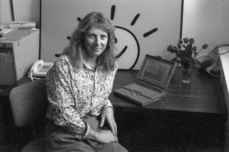 Black and white image of a woman sitting at a desk with a laptop.