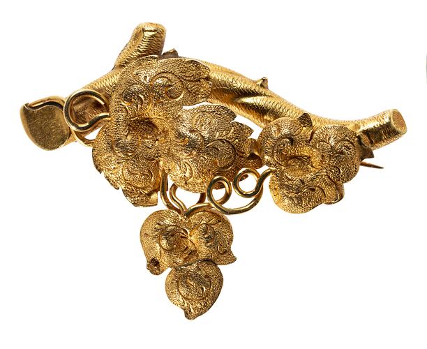 Ornate gold brooch with vine leaves on a branch.