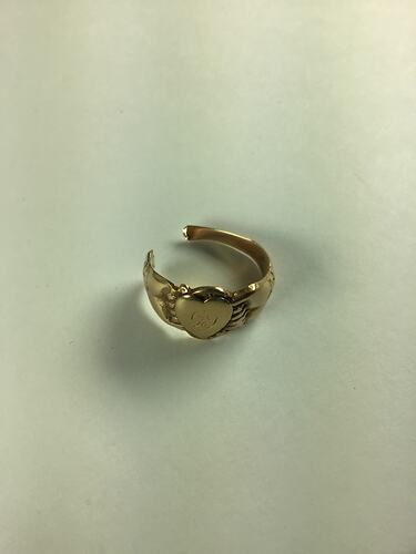 Broken women's gold ring with two clasped hands around a central love heart, inscribed with the worn cursive letters GS.