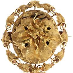 Gold oval locket brooch. Large central vine leaf with flying bird. Oval border surrounded by vine leaves and tendrils. Small bunch of grapes at base.