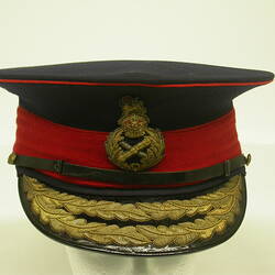 Black cap with red hat band with attached broach and leather visor with gold embroidery.