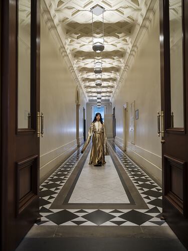 Woman in long dress walking towards camera down an ornate corridor.