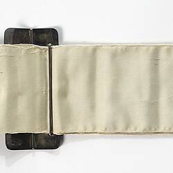 Back of white ribbon sash, buckle, silver fringe and lettering.