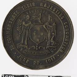 Round bronze coloured medal with coat of arms and text surrounding.