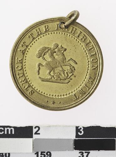 Round gold coloured medal with man on horseback and text surrounding.