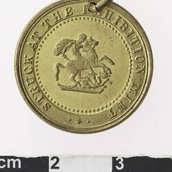 Round gold coloured medal with man on horseback and text surrounding.