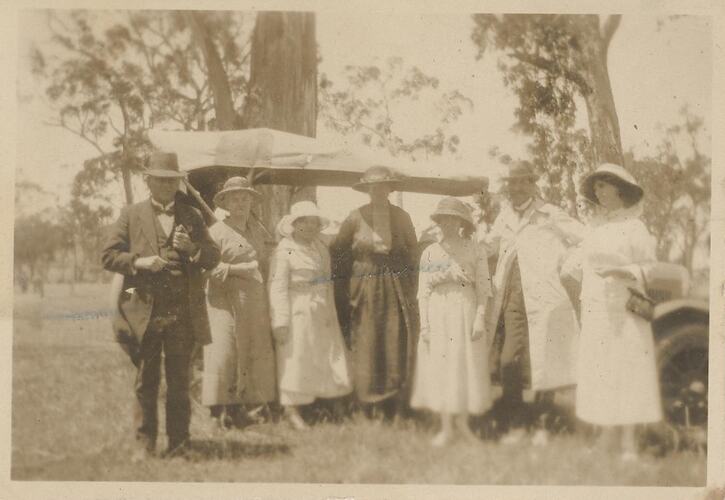 Five woman and two men standing outside in front of trees.