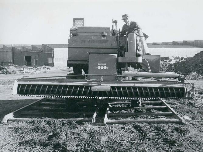 Man driving a harvester fitted with comb front, over a pipe test track.