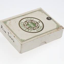 White card box with lid. Central circular logo with text in gold and green ink.