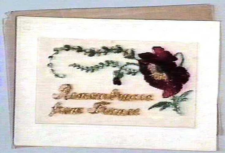 Card on white paper with embroidered red flower and text.