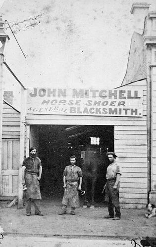 Three men and horse in front of blacksmith building.