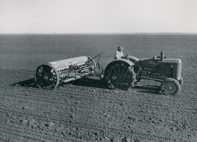 A man driving a tractor connected to a,seed and fertilizer spreader, in a muddy field.