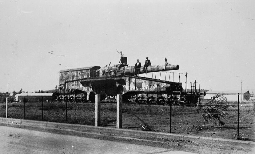 Large railway gun with several people on top at a railway siding.