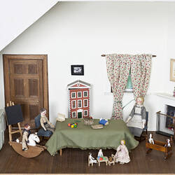 Small painted wooden dolls in a room of a doll house. Room is a nursery with toys and a miniature Pendle Hall.