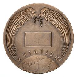 Angel wings frame top of medal. Below a blank inscription plaque. Text and earth at base.