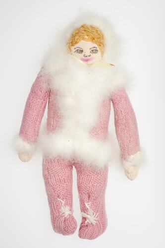 Female cloth doll wearing pink knitted suit with white feather trim.