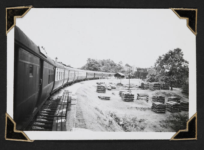Train on tracks, large sacks of wood on ground besides tracks.