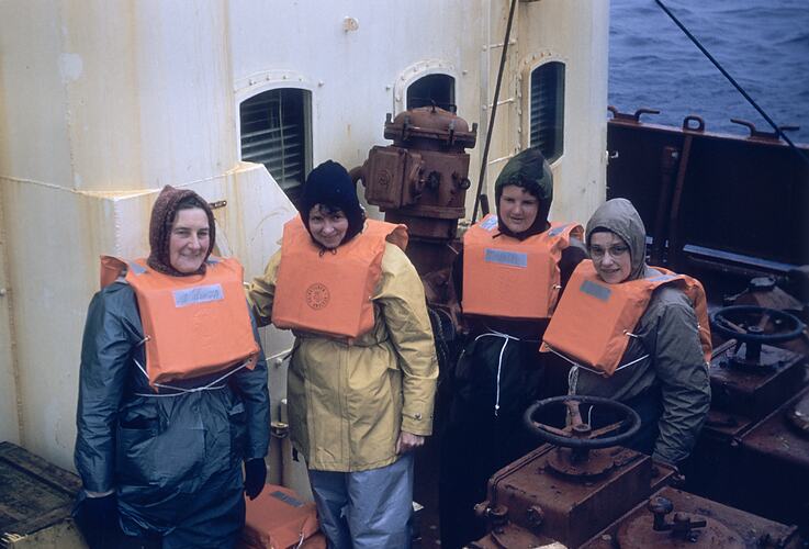 Four women in lifejackets on ship deck.