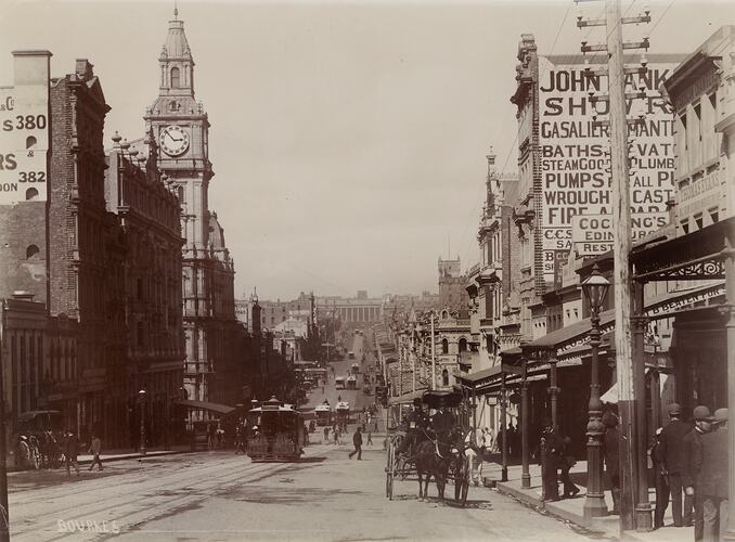 Street view with horsedrawn cart and cable trams. Clocktower at left.