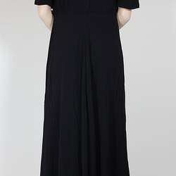 Rear view, long black dress with elbow sleeves.