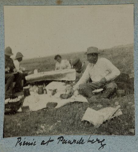 Four men and one woman sitting in field having a picnic.