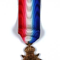 Star shaped medal with crossed swords, wreath and crown and blue, white and red ribbon.