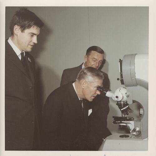 Three men looking at microscope.