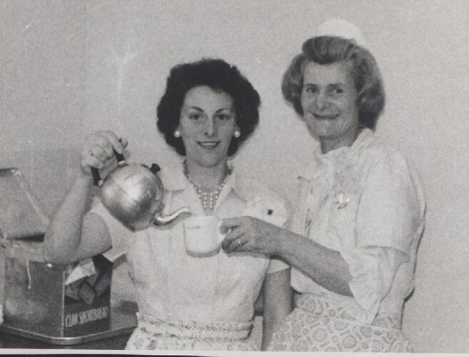 Woman pouring tea into another's cup.
