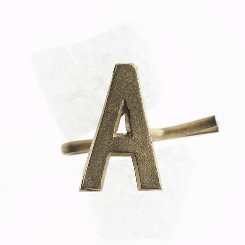 Brass badge in shape of letter A.