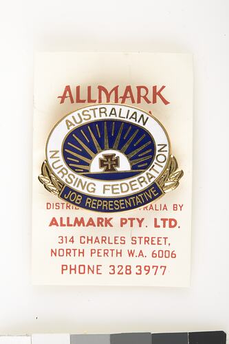 Blue and white oval enamel badge attached to white card with red printing.