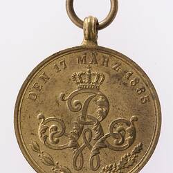 Round medal with ornate central letter R. Text around. Suspension ring at top.