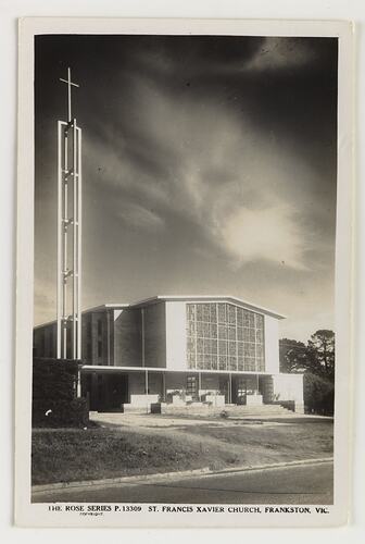Exterior of white church with large central rectangular glass. White cross on metal tower at left.