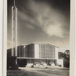 Exterior of white church with large central rectangular glass. White cross on metal tower at left.