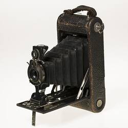 Black camera with leather covering. Folds out with bellows, metal brackets. Front angle view.