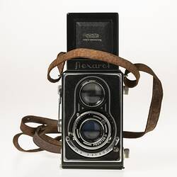 Metal twin lens reflex camera. Body covered in black leather. Leather carry strap.