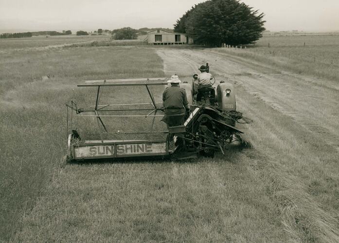 Rear view of a man driving a tractor coupled with a PTO Reaper Binder.