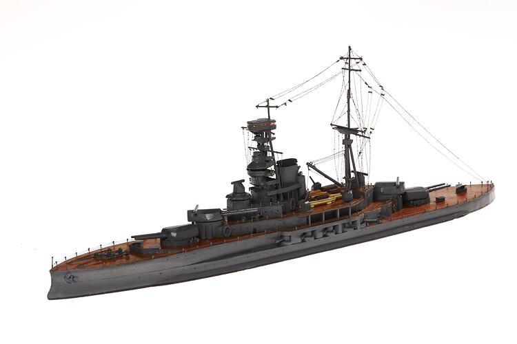 Wooden grey naval ship model with central tower, mast, mounted guns on wooden decks.