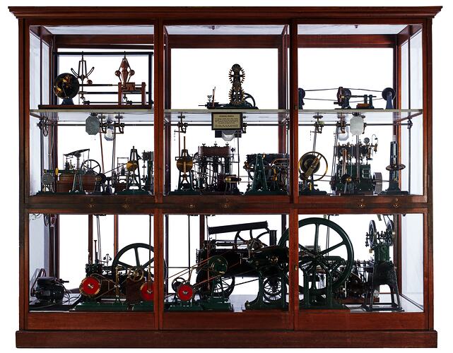 Three level wooden framed glass display case. Contains working models.