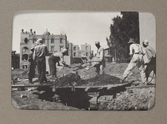 Workmen digging hole near buildings.